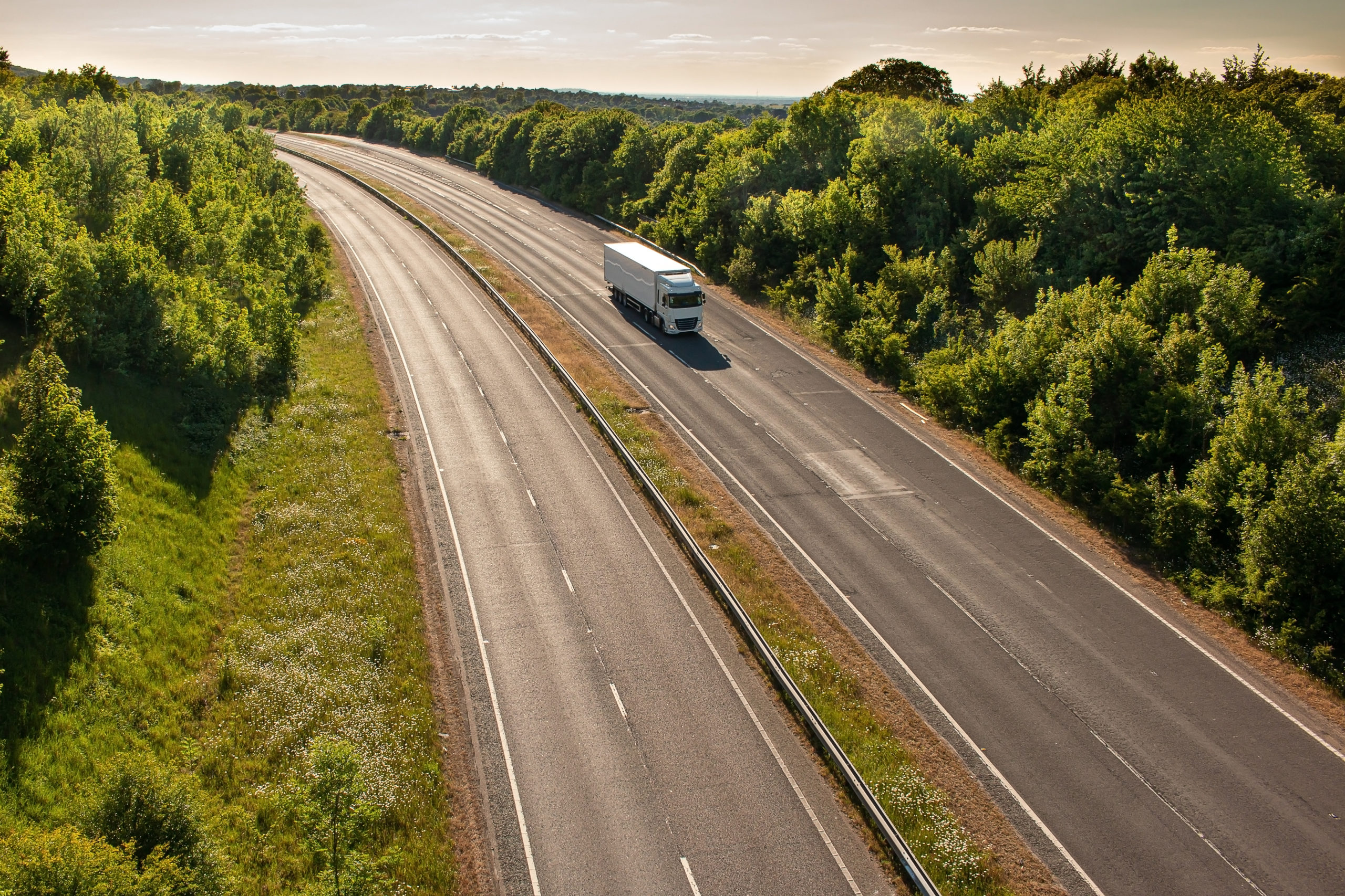 single lorry driving on a road lined with trees and shrubbery
